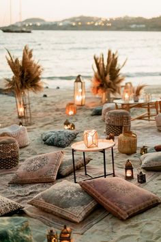 an outdoor seating area with candles and pillows on the beach