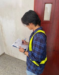 a young boy writing on a piece of paper in front of a red wooden door