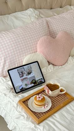 a laptop computer sitting on top of a bed next to a heart shaped pillow and cup