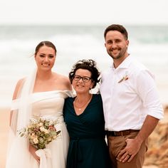 a man and woman standing next to each other on a beach with the ocean in the background