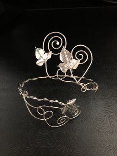 a metal headband with leaves and vines on it's sides, sitting on a black surface