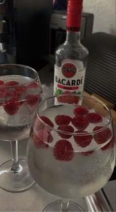 two glasses filled with ice and raspberries next to a bottle of bacardi