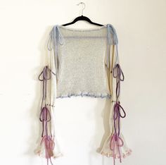 a sweater hanging on a hanger with pink and purple ribbons attached to the top