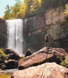 a man standing on top of a large rock next to a waterfall