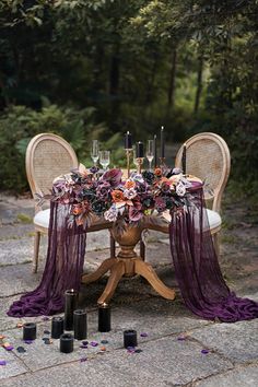 an outdoor table with candles and flowers on it, surrounded by purple draping