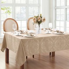 a dining room table set with place settings and flowers in a vase on the table