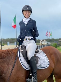 a woman riding on the back of a brown horse next to a green field and flags