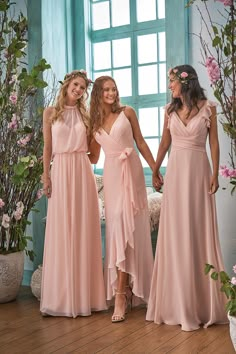 three women in pink dresses standing next to each other with flowers on the wall behind them