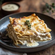 a black plate topped with lasagna covered in cheese and sauce on top of a wooden table