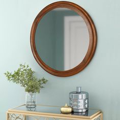 a round mirror on the wall above a table with vases and a bottle next to it