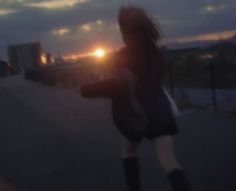 a woman is walking down the street at night with her cell phone in hand and the sun setting behind her