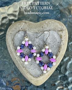 a pair of purple and white beaded earrings sitting on top of a heart shaped rock