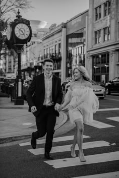 a man and woman are holding hands as they cross the street in front of a clock