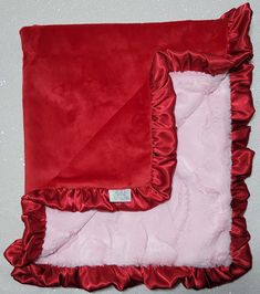 a red and white blanket with ruffles on the bottom is laying next to a pink pillow