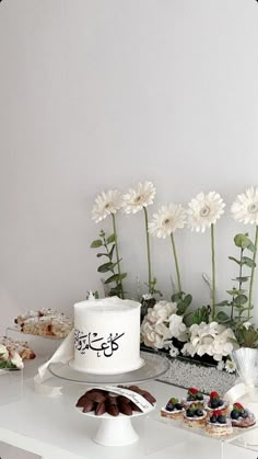 a white cake sitting on top of a table next to flowers and other desserts