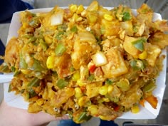 a person holding up a paper plate filled with corn and meat mixture on top of it