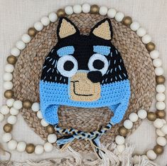 a crocheted hat with a cat on it and beads around the edges, hanging from a wall