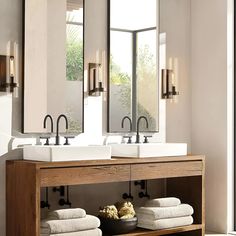 two sinks and mirrors in a bathroom with towels on the shelf under them next to each other