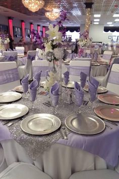 the table is set with silver and white plates, silver napkins, and flower centerpieces