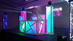 a man standing on top of a stage next to two tall pillars covered in neon lights