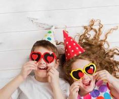 two children wearing party hats and sunglasses laying next to each other on a white wooden floor