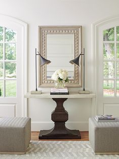 a living room with two chairs, a table and a mirror on the wall above it