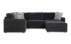 a gray sectional couch with pillows on it and a black foot stool next to it