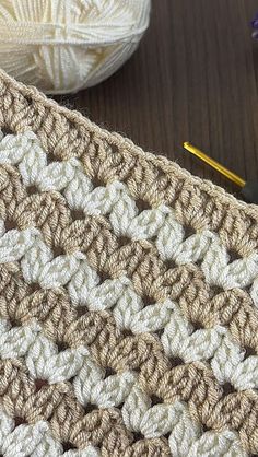 a crocheted blanket sitting on top of a wooden table next to a ball of yarn