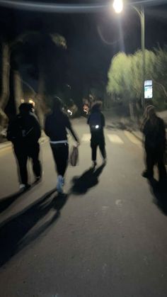 three people walking down the street at night with their backs turned to the camera,