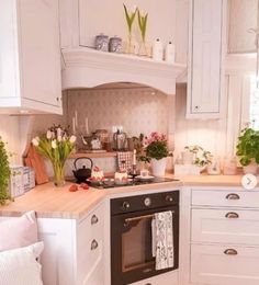 a kitchen with white cabinets and an oven in the center, surrounded by potted plants