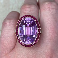 This impressive gemstone ring features a natural 24.10-carat oval-cut kunzite with excellent pink color saturation. Surrounding the center kunzite is a halo of French-cut rubies. The under-gallery is decorated with a lace design and diamonds. This ring is made in 18k yellow gold.
The total approximate ruby weight is 1.20 carats. The total approximate diamond weight is 0.50 carats.
The measurements, including the ruby halo, are 19mm x 25mm.
This ring can be resized to any finger size at no extra Pink Oval Multi-stone Ruby Ring, Pink Oval Ruby Ring With Gemstone Accents, Pink Oval Amethyst Ring, Oval Pink Gemstones With Accent Stones, Formal Oval Kunzite Rings, Fine Jewelry Oval Kunzite Rings, Oval Pink Amethyst Ring With Diamond, Oval Amethyst Gemstone Ring, Pink Oval Amethyst Ring Fine Jewelry