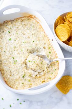 a white casserole dish filled with dip and tortilla chips on the side