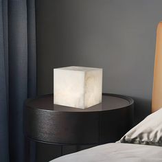 a night stand with a light on top of it next to a bed in a bedroom