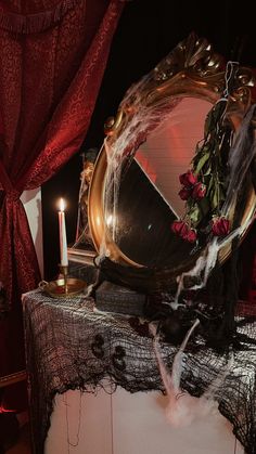 a table with a mirror and candles on top of it in front of a red curtain