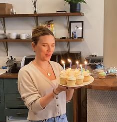 a woman holding a plate with cupcakes on it and lit candles in the middle