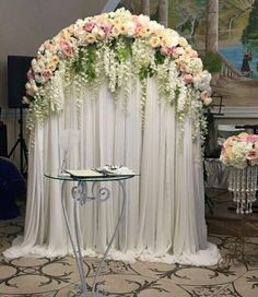 a table with flowers on it in front of a white drape curtain and some chairs