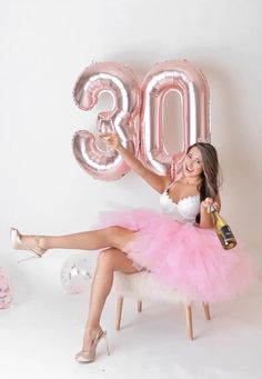 a woman in a pink tutu sitting on a chair holding a bottle and champagne