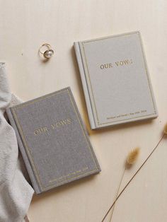 two wedding rings are sitting next to their vows book on a table with some dried flowers