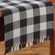 a black and white checkered table runner with tassels on the end, sitting on a wooden chair