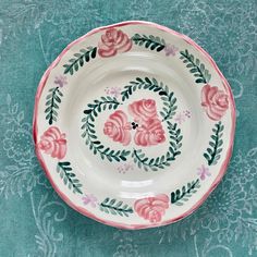 a white plate with pink flowers and green leaves on the rim is sitting on a blue tablecloth