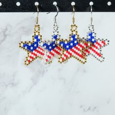 three star shaped beaded earrings hanging from hooks on a marble counter with white and black background