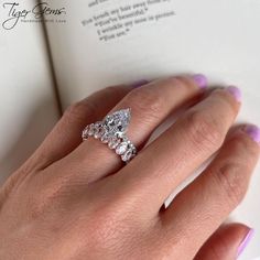 a woman's hand holding an open book with a ring on top of it