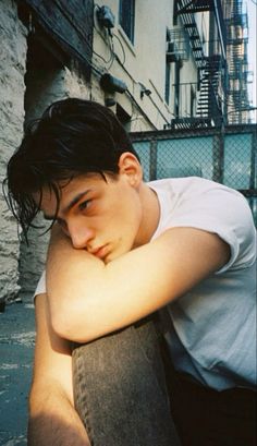 a young man sitting on the ground with his arms folded over his chest and looking at the camera