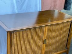 a wooden cabinet sitting on top of a floor next to a white sheet covered wall