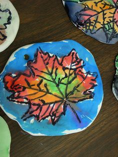 three leaf shaped paper plates on a wooden table with paint and crayons in the background