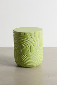 a small green vase sitting on top of a cement floor next to a white wall