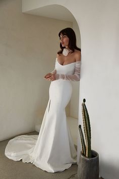 a woman in a white wedding dress leaning against a wall next to a cacti