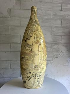 a yellow vase sitting on top of a white table next to a brick wall in the background