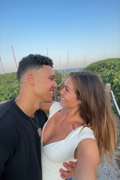 a man and woman standing next to each other in front of green plants with blue sky