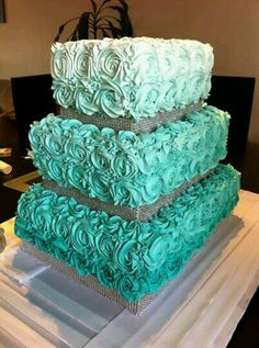 three tiered cake sitting on top of a white table cloth covered in blue frosting